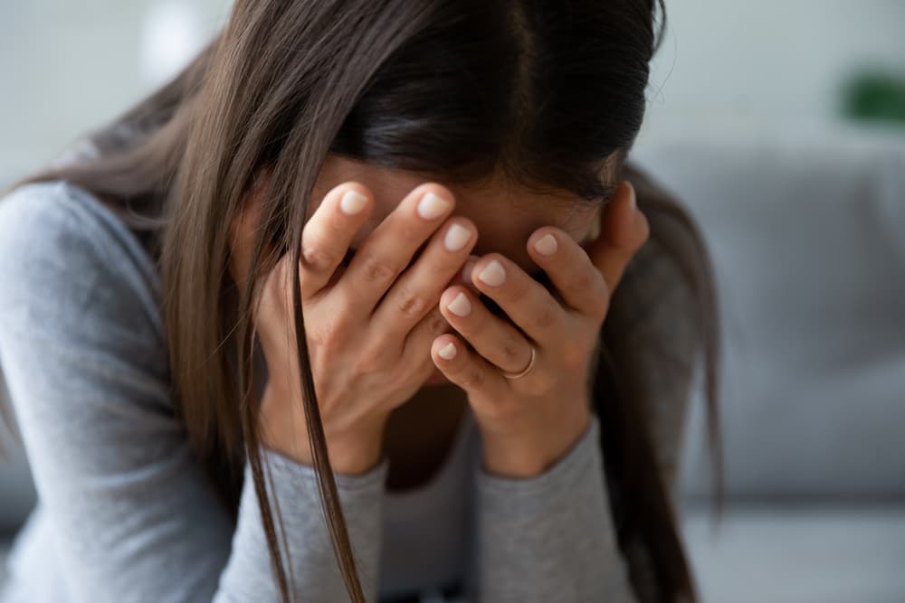 Close up unhappy young woman hiding face in hands, feeling desperate cheated hopeless alone indoors.