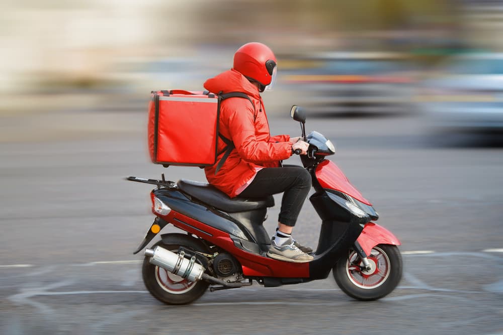 Food delivery moto scooter driver with red backpack behind back is on his way to deliver food.