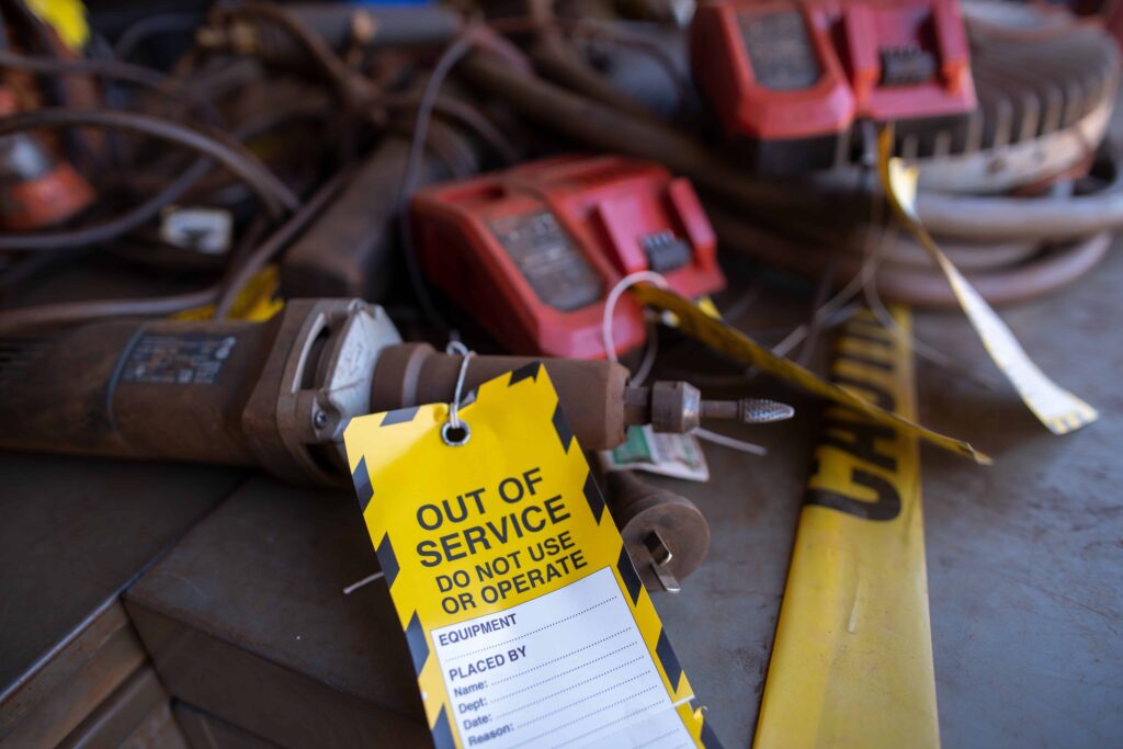 Out-of-service equipment tagged with safety warning labels in a workshop, indicating malfunctioning tools and caution tape.