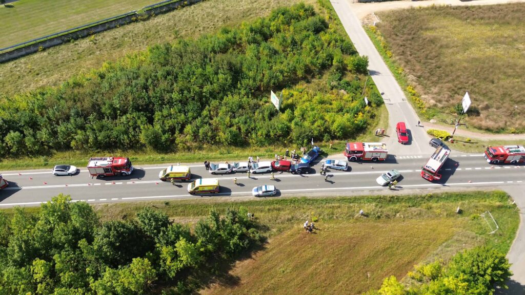 Aerial view of a multi-vehicle accident on a rural road with emergency responders, fire trucks, ambulances, and police at the scene.